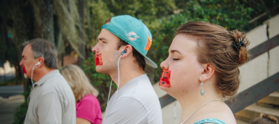 Four people pray silently for the ending of abortion with the word LIFE written across their mouths on red tape.