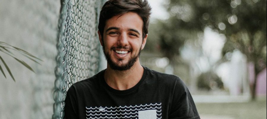 A happy guy leans up against a chain-link fence.